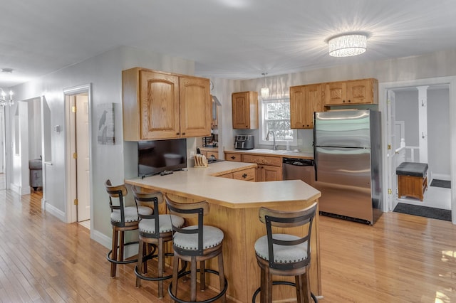 kitchen with a peninsula, light countertops, a sink, light wood finished floors, and appliances with stainless steel finishes