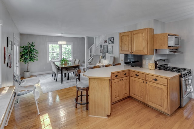 kitchen featuring light wood-style floors, light countertops, a breakfast bar area, range with gas stovetop, and stainless steel microwave