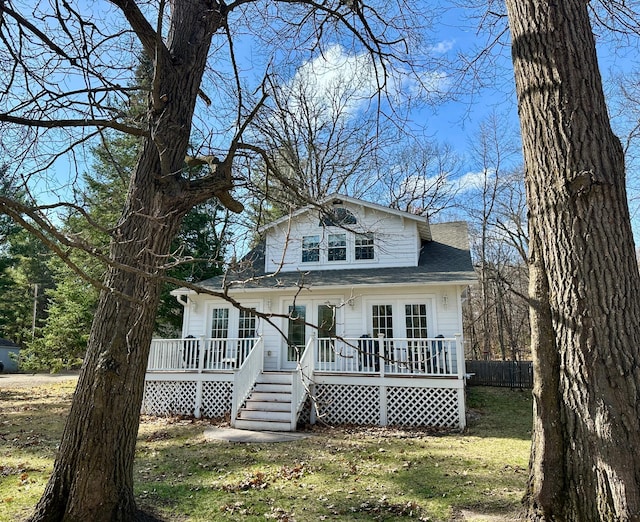 bungalow-style home featuring a deck, fence, a shingled roof, and a front yard