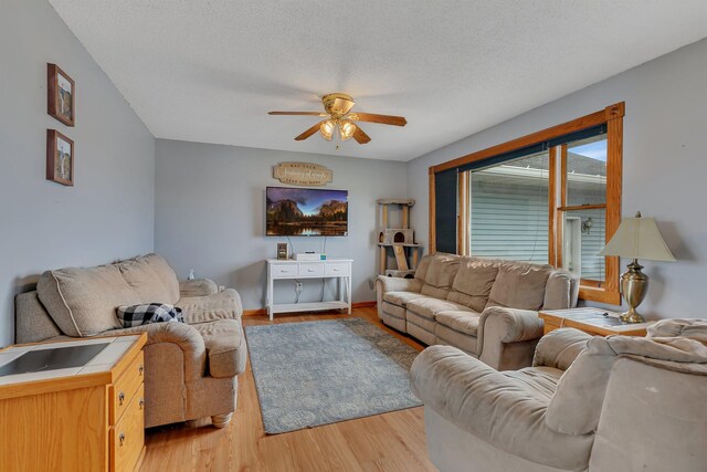 living room with light wood-type flooring, a textured ceiling, ceiling fan, and baseboards