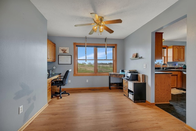 office featuring a textured ceiling, baseboards, a ceiling fan, and wood finished floors