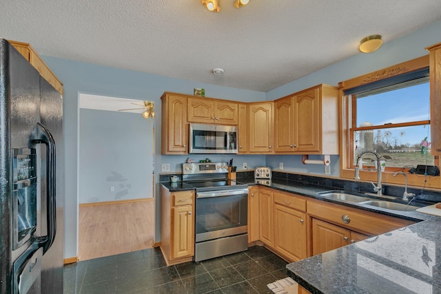 kitchen featuring appliances with stainless steel finishes, granite finish floor, a sink, baseboards, and dark stone counters
