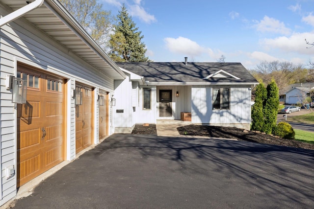 view of front facade with board and batten siding, roof with shingles, and aphalt driveway