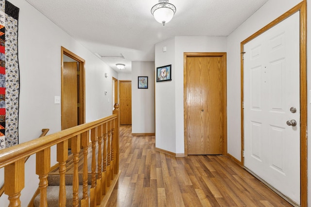 corridor featuring baseboards, light wood finished floors, a textured ceiling, and an upstairs landing