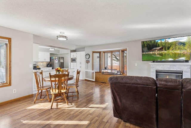 interior space with baseboards, a textured ceiling, light wood finished floors, and a brick fireplace