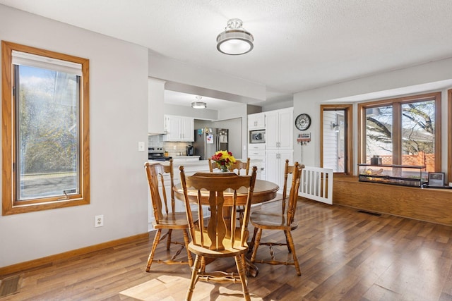 dining space featuring a textured ceiling, baseboards, visible vents, and light wood-style flooring