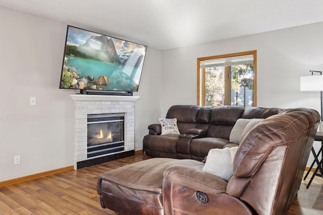 living room featuring baseboards, a brick fireplace, and wood finished floors