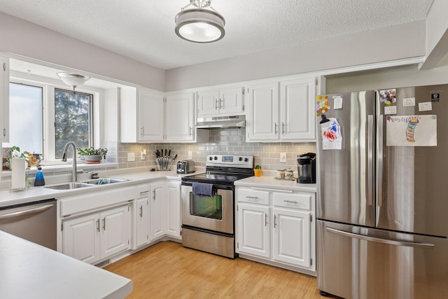 kitchen with under cabinet range hood, stainless steel appliances, white cabinetry, and a sink