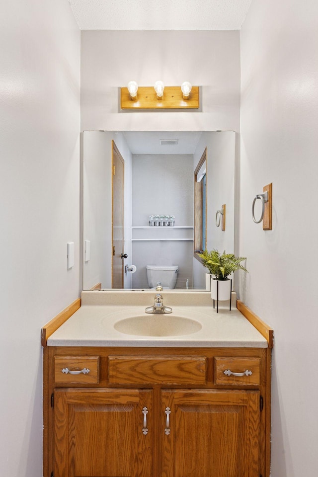 half bath with toilet, visible vents, and vanity