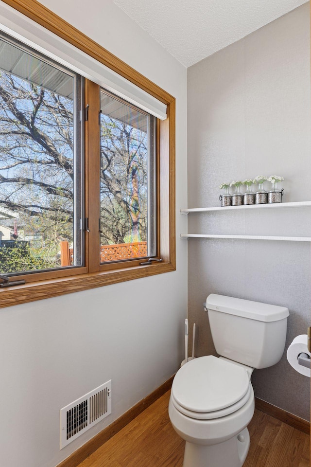 bathroom with baseboards, toilet, wood finished floors, and visible vents