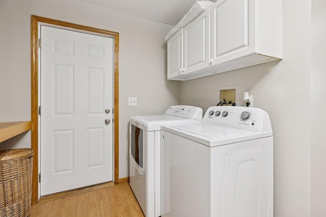 clothes washing area with light wood-style floors, a textured ceiling, cabinet space, and washer and dryer