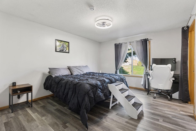 bedroom featuring baseboards, a textured ceiling, and wood finished floors