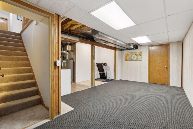 finished below grade area featuring carpet floors, water heater, a drop ceiling, and stairway