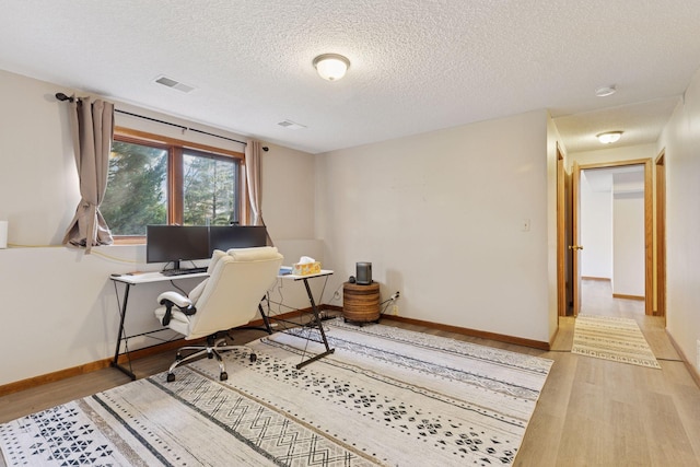 home office with a textured ceiling, baseboards, wood finished floors, and visible vents