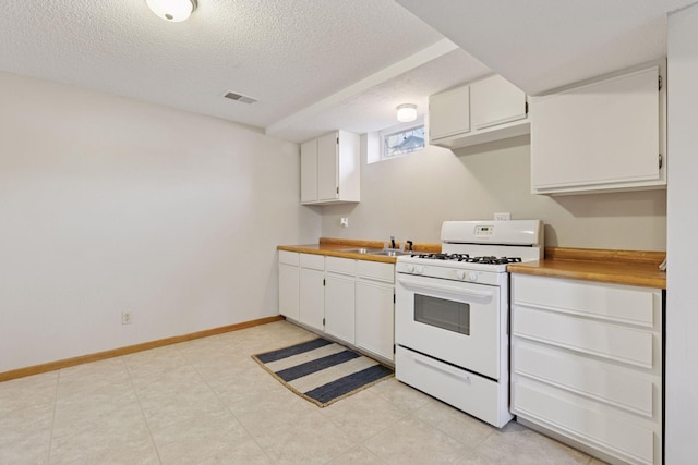 kitchen with white gas range, a textured ceiling, visible vents, light countertops, and white cabinetry