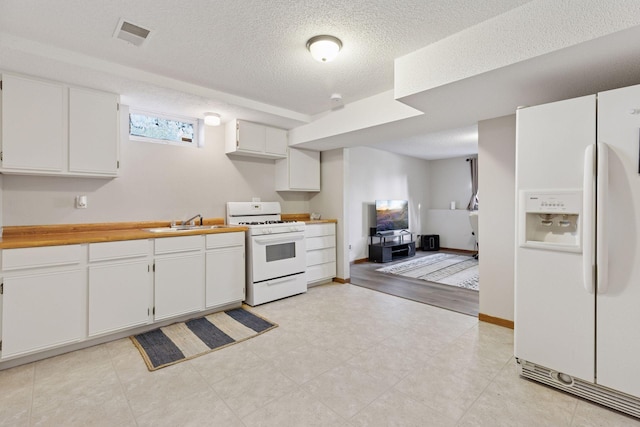 kitchen featuring a textured ceiling, visible vents, a sink, white cabinets, and white appliances