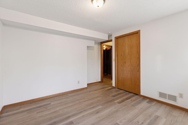 empty room featuring visible vents, a textured ceiling, light wood-style floors, and baseboards