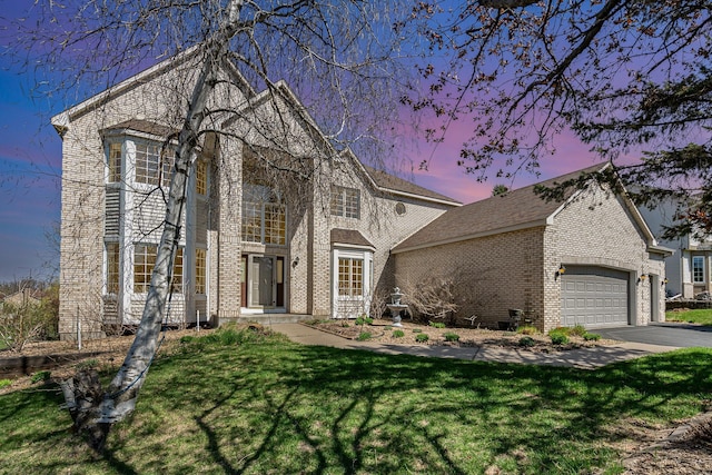 traditional-style house featuring a yard, brick siding, an attached garage, and aphalt driveway