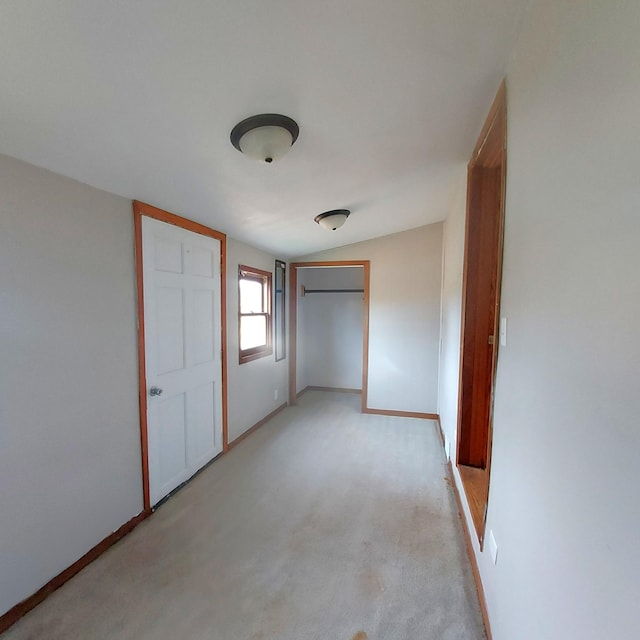 unfurnished bedroom with baseboards, lofted ceiling, a closet, and light colored carpet