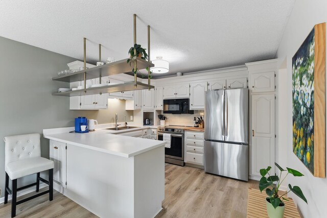kitchen with a sink, a peninsula, white cabinetry, and appliances with stainless steel finishes