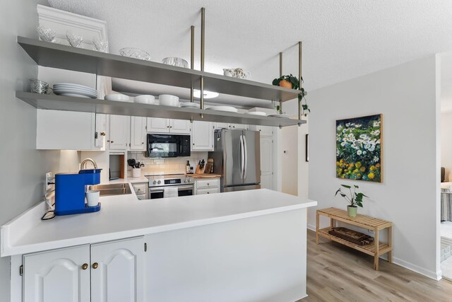 kitchen featuring black microwave, open shelves, a peninsula, and freestanding refrigerator