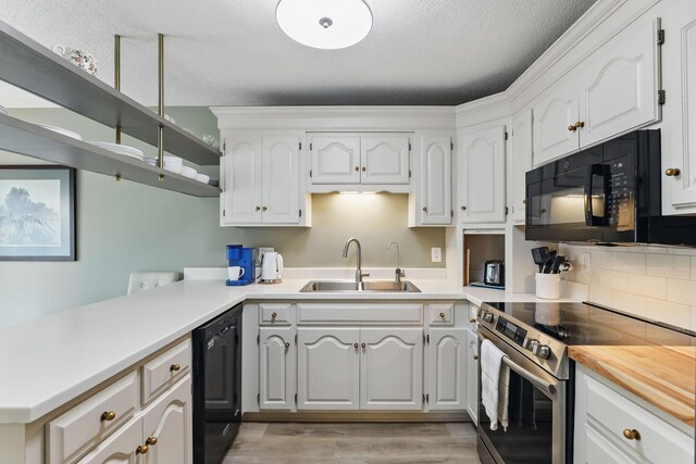 kitchen with a peninsula, light wood-type flooring, white cabinets, a sink, and black appliances