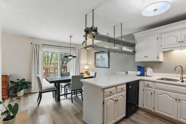 kitchen with white cabinets, a sink, black dishwasher, a peninsula, and light wood-type flooring