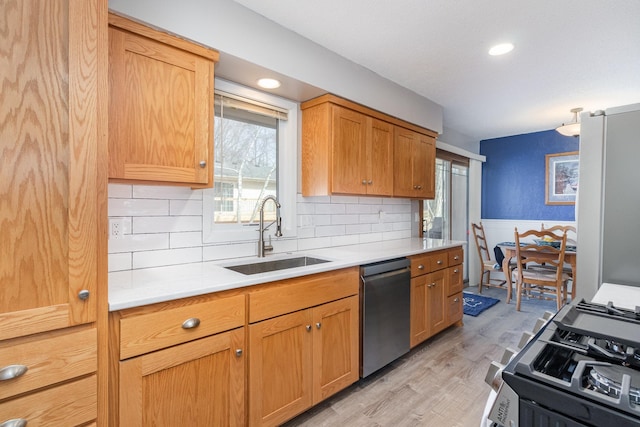 kitchen featuring range with gas cooktop, dishwasher, a sink, light countertops, and freestanding refrigerator