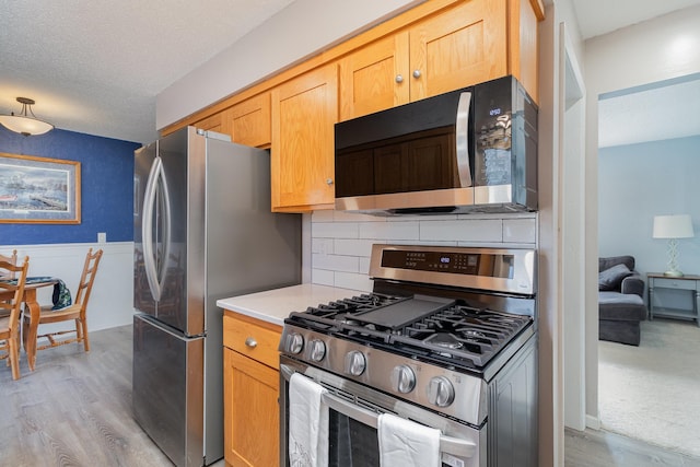 kitchen featuring decorative backsplash, appliances with stainless steel finishes, light countertops, a wainscoted wall, and light wood-style floors
