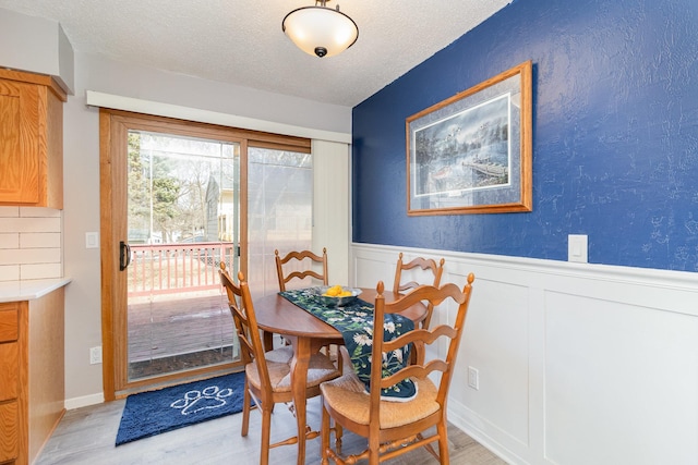 dining area featuring wainscoting, light wood finished floors, and a textured ceiling