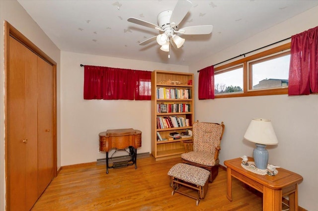 living area with baseboards, a ceiling fan, a baseboard heating unit, and light wood-style flooring