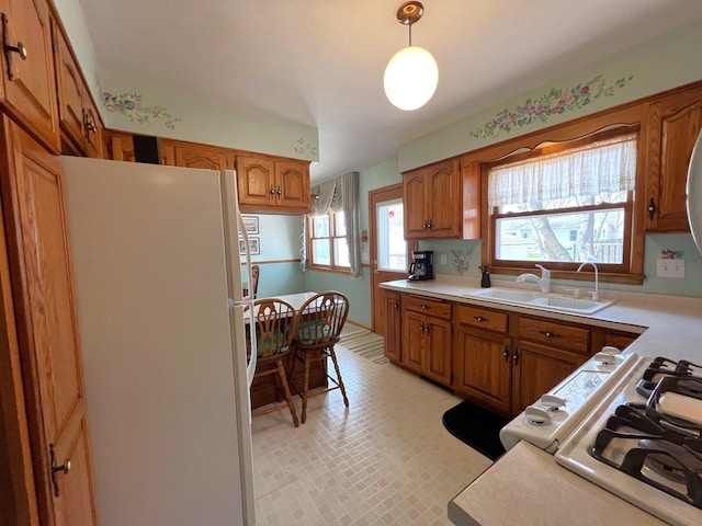 kitchen with freestanding refrigerator, a sink, brown cabinetry, light countertops, and pendant lighting