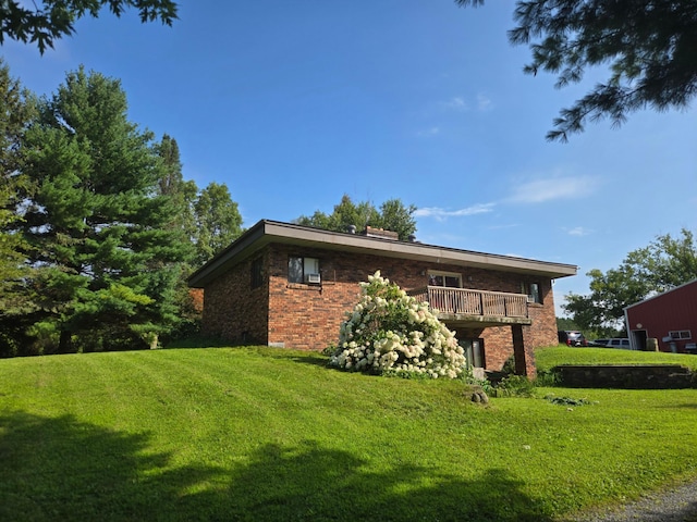 view of side of property featuring a lawn, brick siding, a chimney, and a balcony