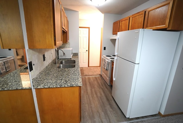 kitchen featuring brown cabinetry, white appliances, dark wood-style floors, under cabinet range hood, and a sink