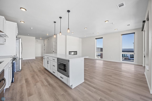 kitchen with white cabinets, appliances with stainless steel finishes, light wood finished floors, a center island, and visible vents