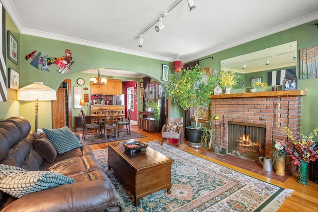 living area with track lighting, arched walkways, wood finished floors, a chandelier, and ornamental molding