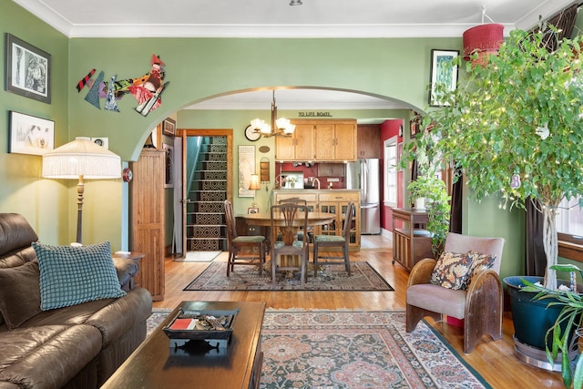 living room with a chandelier, ornamental molding, arched walkways, and light wood-type flooring