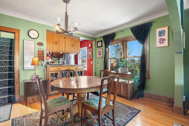 dining area with a chandelier, ornamental molding, light wood-type flooring, and baseboards