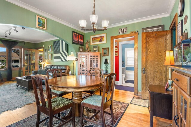 dining area featuring arched walkways, light wood finished floors, a chandelier, and ornamental molding