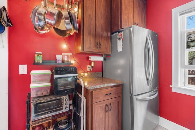 kitchen featuring freestanding refrigerator, baseboards, brown cabinetry, and a toaster
