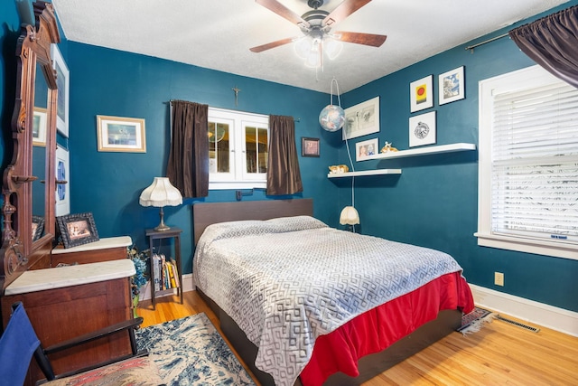 bedroom featuring baseboards, a ceiling fan, visible vents, and wood finished floors