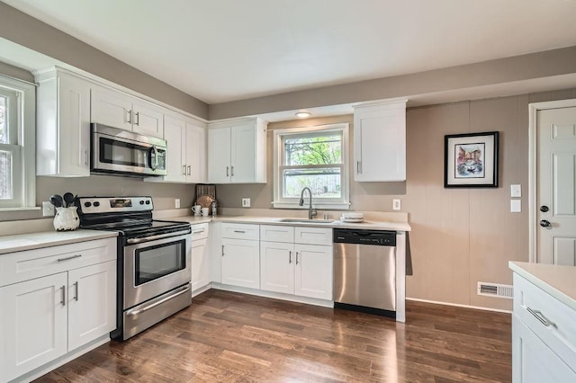 kitchen featuring appliances with stainless steel finishes, a sink, light countertops, and dark wood-type flooring