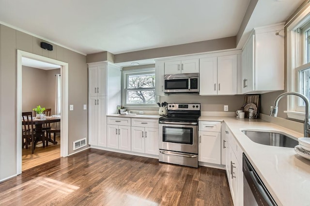 kitchen featuring stainless steel appliances, a sink, white cabinets, light countertops, and dark wood-type flooring