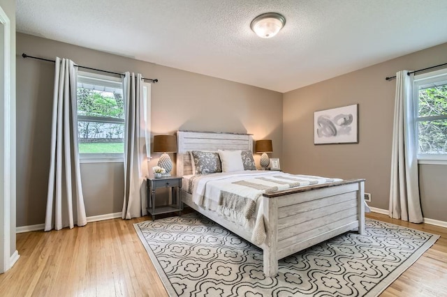 bedroom with light wood finished floors, baseboards, and a textured ceiling