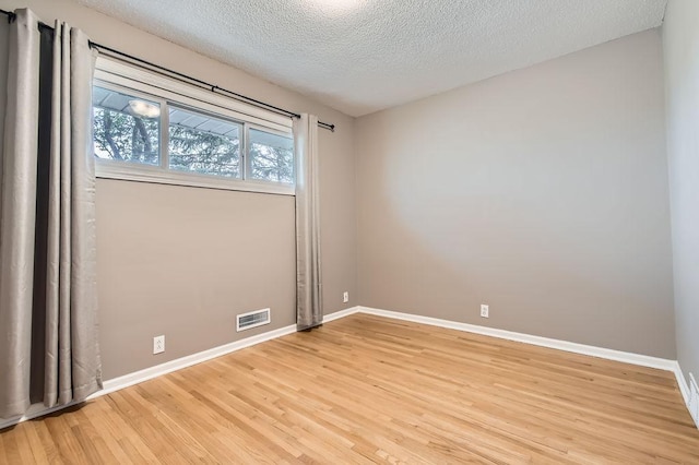 spare room with light wood-style flooring, a textured ceiling, and baseboards