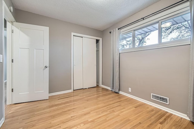 unfurnished bedroom featuring light wood-style floors, baseboards, a textured ceiling, and a closet