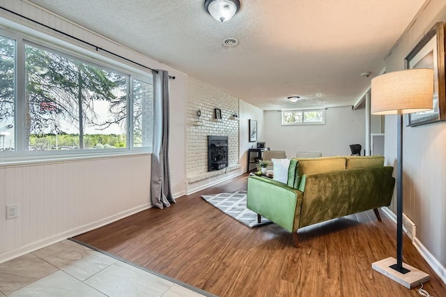 living area with a brick fireplace, baseboards, a textured ceiling, and wood finished floors