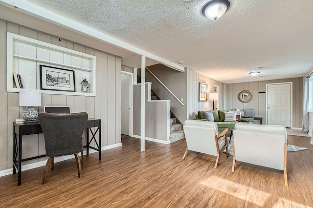 living area with a textured ceiling, wood finished floors, stairs, baseboards, and wood walls