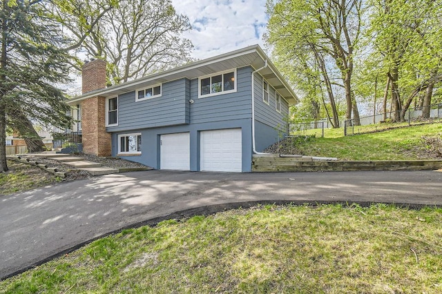 view of side of home with asphalt driveway, a chimney, an attached garage, and stucco siding