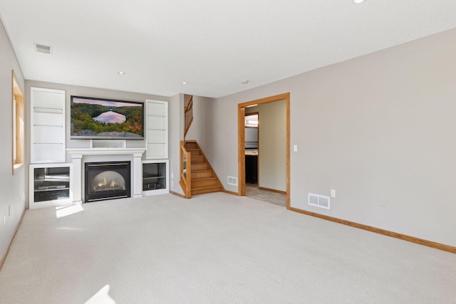 unfurnished living room with visible vents, carpet flooring, a glass covered fireplace, and stairway
